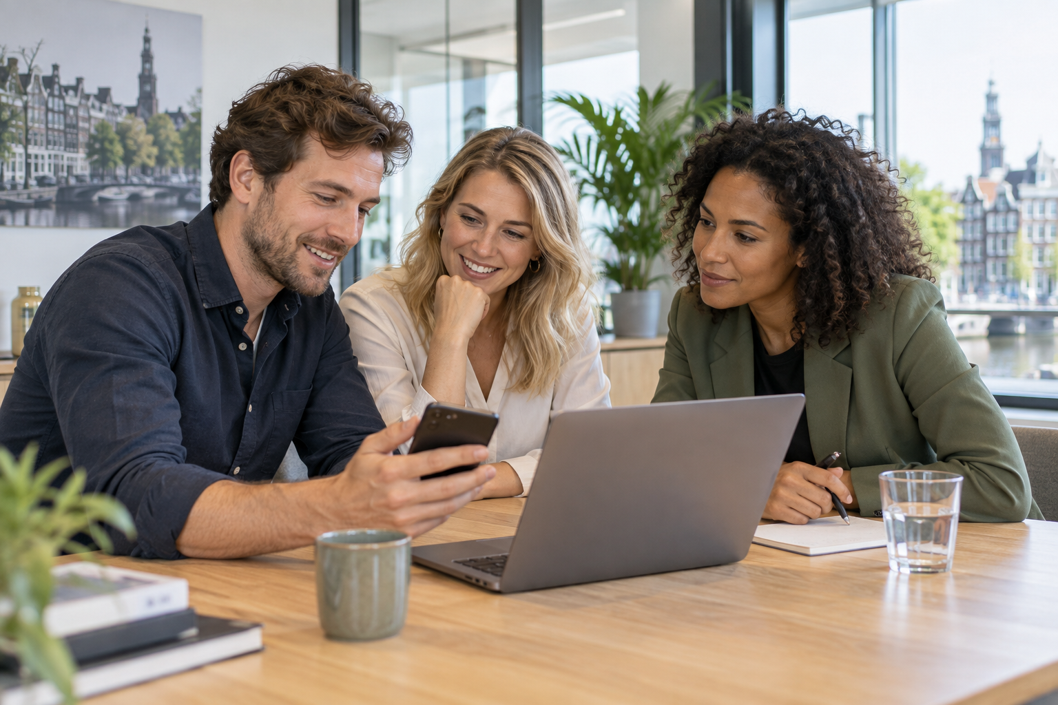 Drie collega’s bekijken samen een smartphone aan een vergadertafel